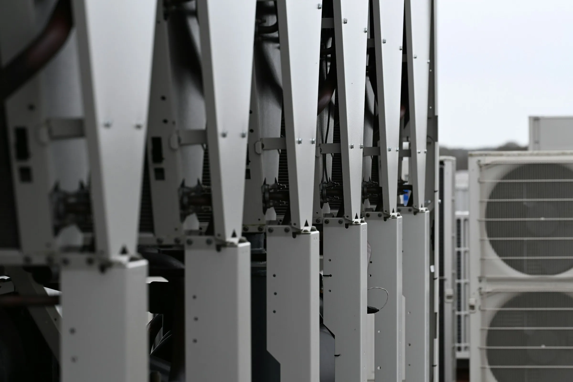 A row of condenser units with fan cowls and finned coils on a rooftop plant deck